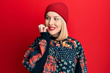 Kışın yün şapka takan genç sarışın kadın gergin ve gergin görünüyor. Ağzı tırnak yiyen ellerle. anksiyete. 