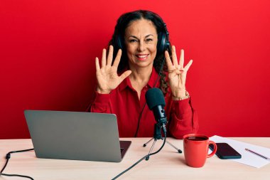 Radyo stüdyosunda çalışan orta yaşlı güzel bir kadın dokuz numaralı parmaklarını gösterip işaret ederken kendine güvenen ve mutlu bir şekilde gülümsüyor.. 