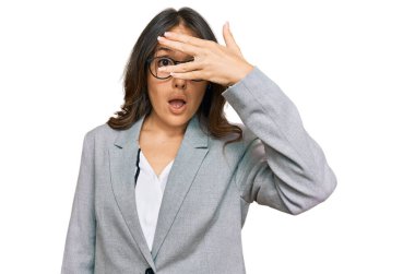 İş kıyafetleri giymiş genç esmer kadın şok içinde yüzünü ve gözlerini kapayarak utangaç ifadesiyle parmaklarının arasından bakıyor.. 