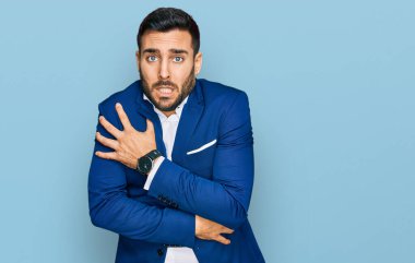 İş ceketi giymiş genç İspanyol bir adam. Yüzünde üzgün ve şok ifadesiyle kış soğuğu için titriyor ve donuyor. 