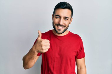 Gündelik kıyafetler giyen genç İspanyol adam elleriyle mutlu bir jest yapıyor. Kameraya bakıp başarıyı gösteren ifade. 