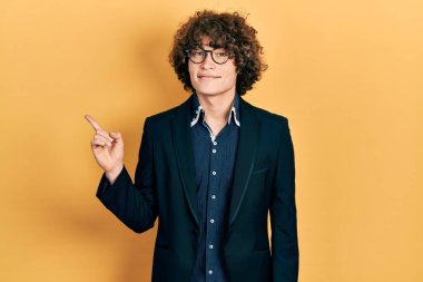 İş ceketi ve gözlük takan yakışıklı genç adam mutlu bir şekilde gülümsüyor. 