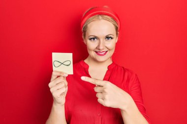 Sarışın genç kadın sonsuz bir sembol tutuyor. Gülümsüyor, mutlu bir el ve parmak ile işaret ediyor. 