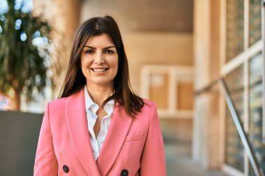 Zarif bir ceket giyen güzel İspanyol iş kadını şehirde mutlu bir şekilde gülümsüyor.