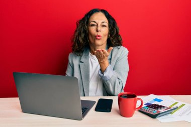 Ofiste çalışan orta yaşlı güzel bir kadın bir fincan kahve içerken kameraya bakıyor ve havada bir öpücük savuruyor güzel ve seksi. aşk ifadesi. 