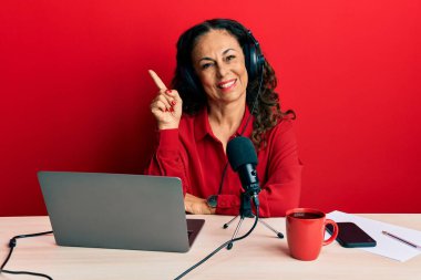 Güzel orta yaşlı bir kadın radyo stüdyosunda çalışıyor. Yüzünde kocaman bir gülümseme var. Elleri ve parmakları kameraya bakıyor.. 