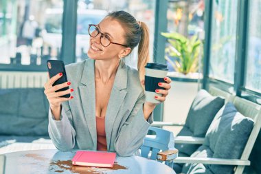 Genç sarışın iş kadını akıllı telefon kullanıyor ve kahve içiyor..