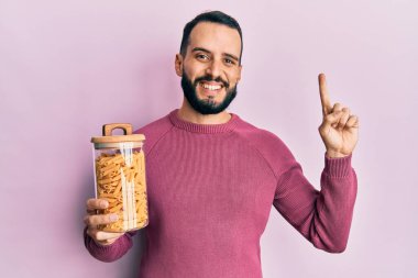 Sakallı genç adam elinde makarna kavanozuyla gülümseyen bir fikir ya da soru işareti ile gülümseyen mutlu yüzlü, bir numara 