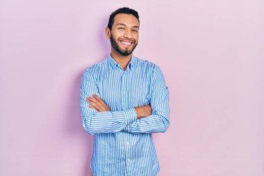 Sakallı, sıradan mavi tişörtlü, mutlu yüzlü, kollarını kavuşturup kameraya bakan İspanyol bir adam. pozitif kişi. 