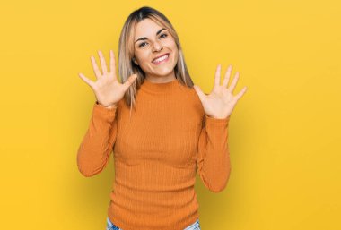 Gündelik giysiler giyen genç beyaz kadın on numarayı gösterip işaret ederken kendinden emin ve mutlu bir şekilde gülümsüyor.. 