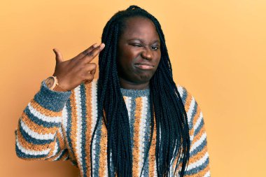 Saçları örgülü genç siyahi bir kadın, günlük kışlık süveter giyiyor ve kendini vuruyor. Elini ve parmaklarını silah gibi kullanıyor. İntihar jesti.. 