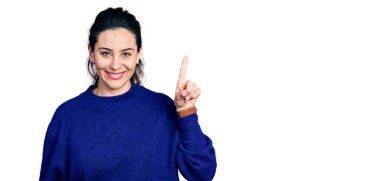 Genç İspanyol kadın gündelik kıyafetler giyip bir numarayı gösterip işaret ederken kendinden emin ve mutlu bir şekilde gülümsüyor.. 