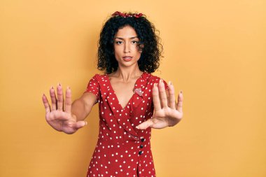 Yazlık elbise giyen genç Latin kız avuç içi hareketlerini durduruyor, kızgın ve hayal kırıklığı dolu bir ifade takınıyor. 