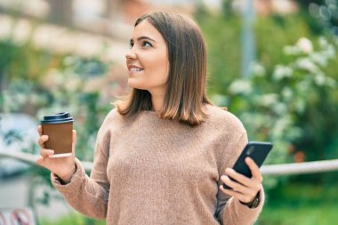 Genç İspanyol kadın akıllı telefon kullanıyor. Parkta kahve içiyor.