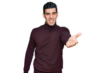 Yakışıklı, balıkçı yaka kazak giyen yakışıklı bir adam dostça gülümseyerek selamlama ve hoş geldin diyor. başarılı iş. 