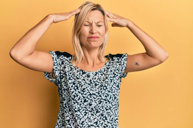 Orta yaşlı beyaz kadın, elleri kafasında günlük kıyafetler giyiyor, stres yüzünden baş ağrısı çekiyor. migren ağrısı. 