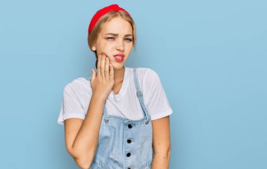 Günlük kıyafetler giyen beyaz bir kız diş ağrısı ya da diş hastalığından dolayı ağızlarına acı dolu bir ifadeyle dokunuyor. dişçi 