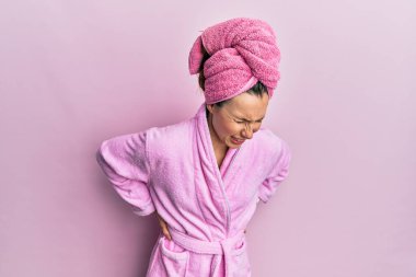 Banyo havlusu şapkası ve bornoz takan genç sarışın kadın sırt ağrısı çekiyor, elleriyle dokunuyor, kas ağrısı çekiyor. 