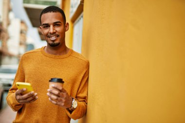 Genç Afrikalı Amerikalı adam akıllı telefon kullanıyor. Şehirde kahve içiyor..