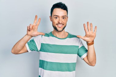 Gündelik kıyafetler giyen genç İspanyol adam sekiz numarayı gösterip işaret ederken kendinden emin ve mutlu bir şekilde gülümsüyor.. 