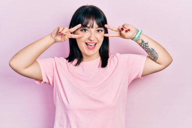 Gündelik kıyafetler giyen genç İspanyol kadın barış sembolü yapıyor. Yüzünde parmaklar, gülümseyerek zaferi gösteriyor. 