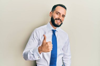 Sakallı, iş kravatlı, mutlu bir el hareketi yapan genç bir adam. Kameraya bakıp başarıyı gösteren ifade. 