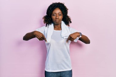 Genç Afro-Amerikan kadın spor giysisi ve havlu giymiş üzgün ve üzgün görünüyor, yönünü parmaklarıyla gösteriyor, mutsuz ve depresif.. 