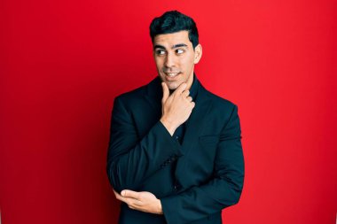 Eli çenesinde iş kıyafetleri içinde soru soran yakışıklı İspanyol bir adam, düşünceli bir ifade. Düşünceli bir yüzle gülümsüyor. şüphe kavramı. 