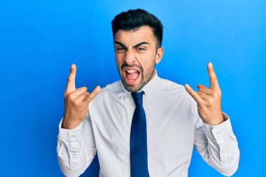 İş kıyafetleri giymiş, çılgın bir ifadeyle bağıran İspanyol genç adam elleri havada rock sembolü yapıyor. Müzik yıldızı. ağır kavram. 