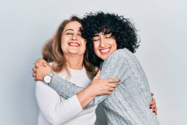 Genç esmer kadın ve yaşlı kadın soyutlanmış arka planda duruyorlar. Kız ve anne, mutlu bir aile gibi sarılıp kaynaşıyorlar.