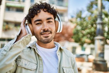 Yakışıklı, sakallı, neşeli, güneşli bir günde kulaklık takan bir İspanyol.