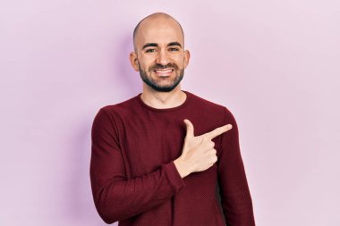 Yüzünde mutlu ve doğal bir ifade olan, elleri ve parmaklarıyla işaret eden, güler yüzlü, sıradan kıyafetler giyen genç kel bir adam. 