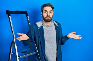 Kafkas sakallı, merdivenden aşağı düşmüş, elleri ve kolları havada, kafası karışmış bir adam. şüphe kavramı. 