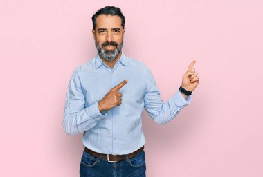 Sakallı, iş gömleği giyen, gülümseyen ve kameraya bakan orta yaşlı bir adam. İki eli ve parmakları yanda.. 