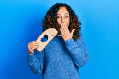 Orta yaşlı İspanyol kadın elinde kalp şeklinde ekmek tutuyordu. Ağzı elle kaplıydı. Şok olmuştu ve hata yapmaktan korkuyordu. şaşırmış ifade 