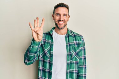 Sakallı, sıradan giyinen, dört numarayı gösteren ve gülümseyen yakışıklı bir adam. Kendinden emin ve mutlu.. 