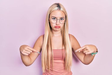 Sıradan kıyafetler giyen genç sarışın kız üzgün ve üzgün görünüyor, parmaklarıyla yön gösteriyor, mutsuz ve depresif.. 