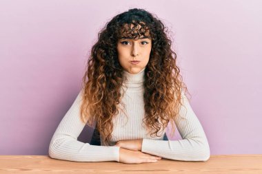 Gündelik kıyafetler giyen genç İspanyol kız masada oturmuş komik suratıyla yanaklarını şişiriyor. Havayla şişmiş ağız, çılgın bir ifade.. 