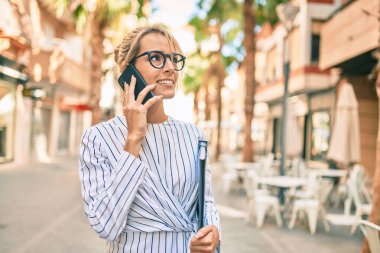 Sarışın bir iş kadınının elinde klasör var ve şehirdeki akıllı telefondan konuşuyor..