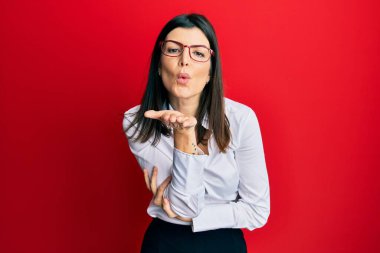 İş gömleği giyen ve gözlüklü genç İspanyol kadın kameraya bakıp havada el sallayarak öpüşüyor. Güzel ve seksi. aşk ifadesi. 