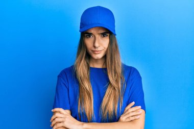 Teslimat üniforması giyen genç İspanyol bir kadın. Kuşkucu ve gergin. Yüzünde çapraz kollu tasvip etmeyen bir ifade var. negatif kişi. 