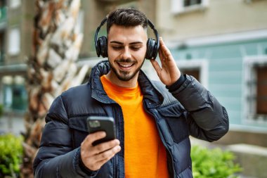 Yakışıklı, sakallı, neşeli, kendine güvenen, kışlık palto giyen, akıllı telefondan müzik dinleyen bir İspanyol.