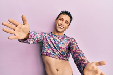 Makyaj elbisesi giymiş yakışıklı bir adam kameraya bakıp sarılmak için kollarını açmış gülümsüyor. Mutluluğu kucaklayan neşeli bir ifade.. 