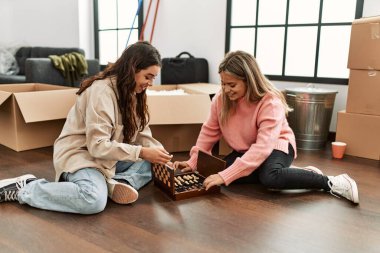 Genç çift yeni evinde yerde oturup satranç oynarken mutlu bir şekilde gülümsüyor..