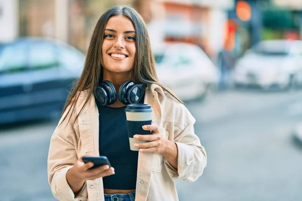 Genç İspanyol kız akıllı telefon kullanıyor ve parktaki kahveleri içiyor. Şehirde..