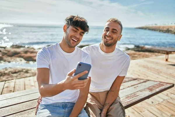 年轻的同性恋夫妇在海滩散步时 用智能手机开心地笑着 — 图库照片