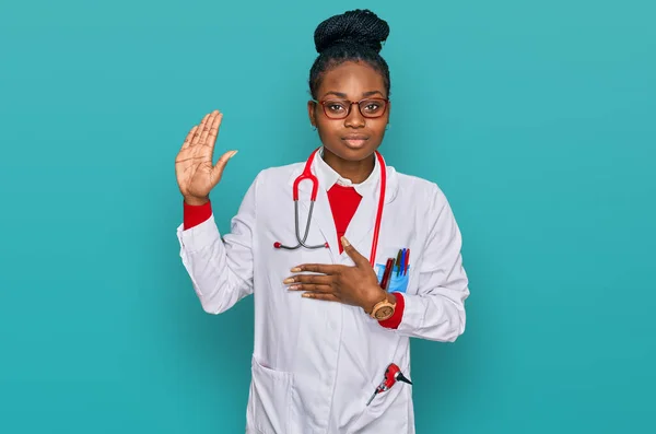 Young african american woman wearing doctor uniform and stethoscope swearing with hand on chest and open palm, making a loyalty promise oath