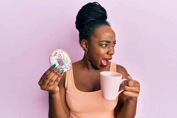 Mujer Afroamericana Joven Comiendo Donut Tomando Café Enojado Loco Gritando —  Fotos de Stock