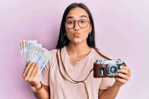 Young asian woman holding vintage camera and swedish krona looking at the camera blowing a kiss being lovely and sexy. love expression.
