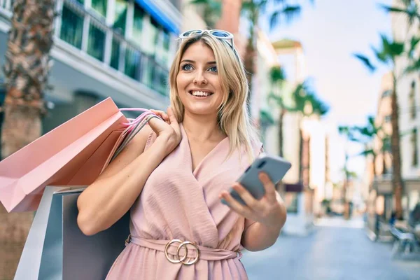 Genç Sarışın Kadın Gülümsüyor Alışveriş Torbaları Tutuyor Şehirde Akıllı Telefon — Stok fotoğraf